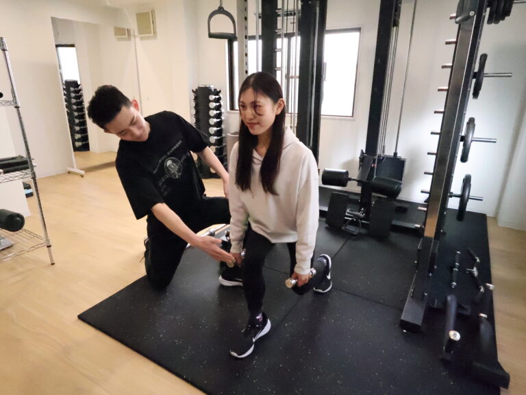 トレーナーの指導でスクワットをする女性